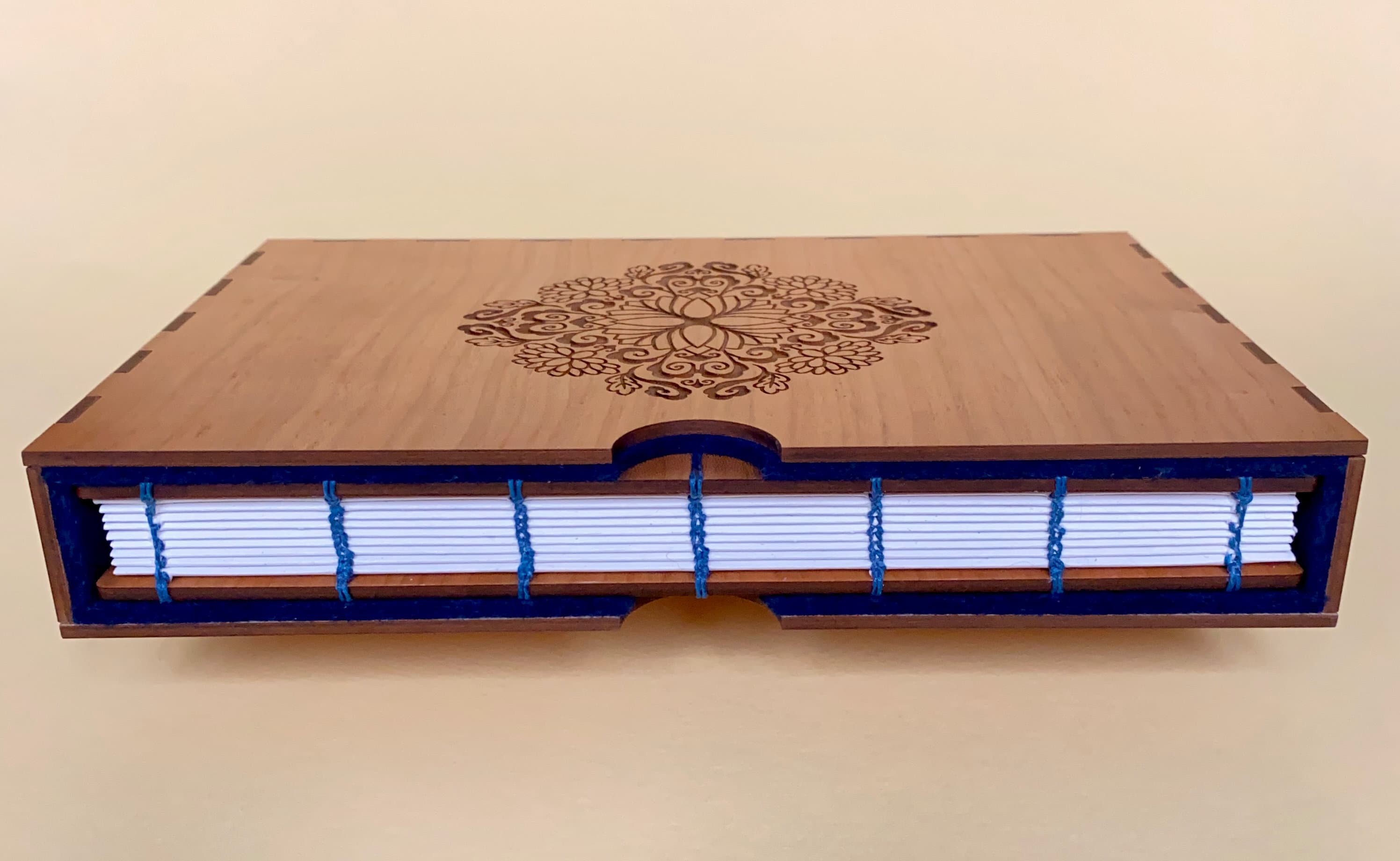 A fondfolio book in a slipcase lays on its side horizontally with the open end of the case facing the camera. The case is made from cherry wood and the background is a pale yellow. The case is lined with cobalt blue felt.