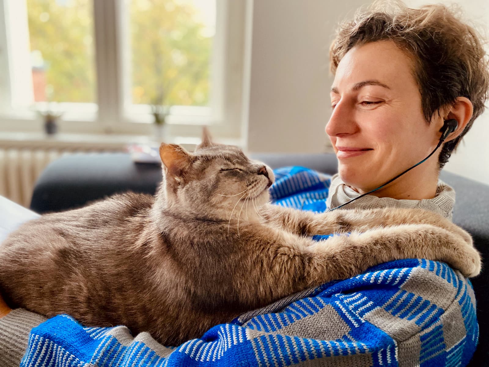 My grey tabby cat minou laying on me, having inserted himself between me and my laptop. I am smiling at him and he seems to be smiling at me, paws draped over my shoulder.