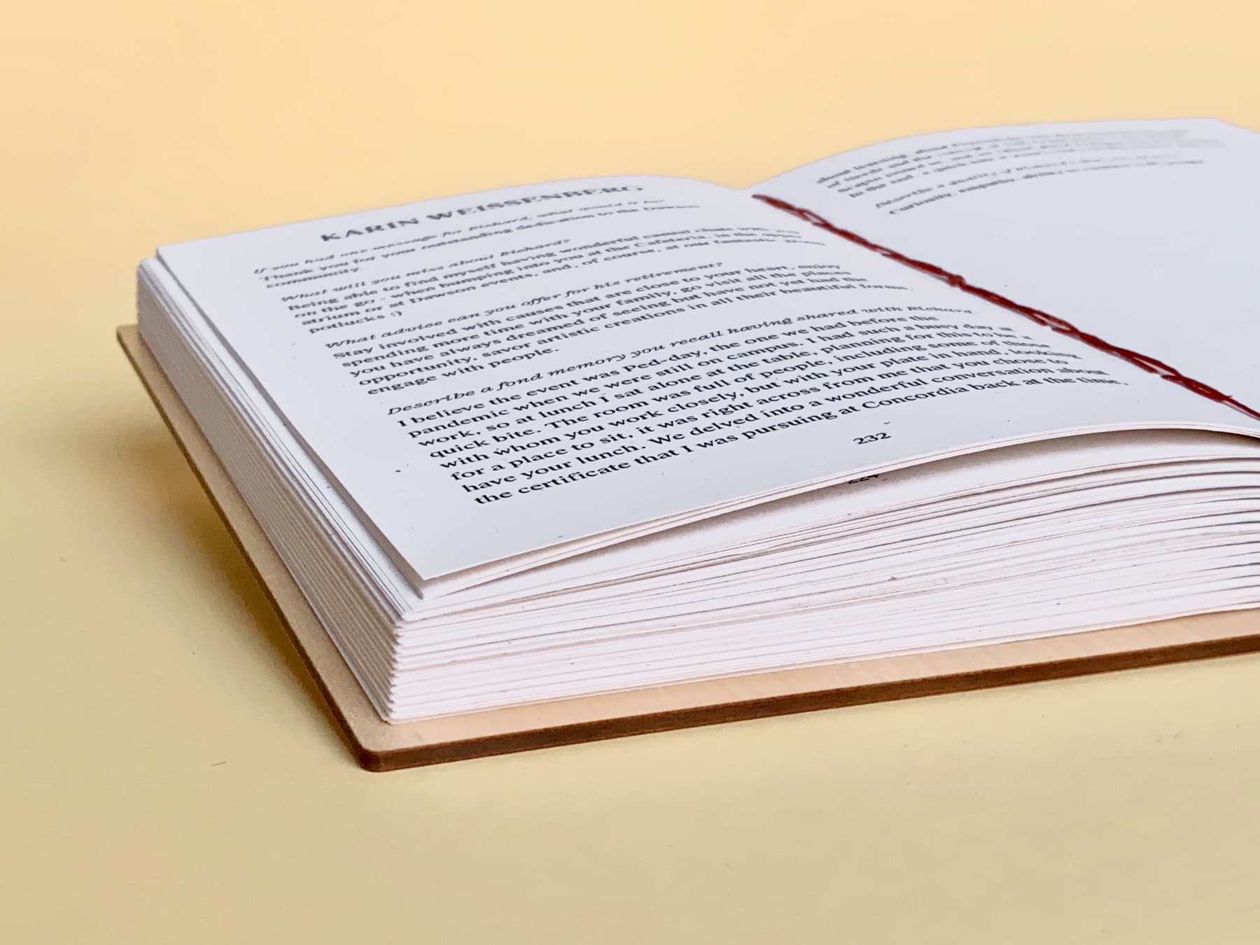 An open coptic bound Fondfolio lies flat and at an angle across a pale yellow background. The cover is maple wood and the thread that binds it is a warm rusty red.