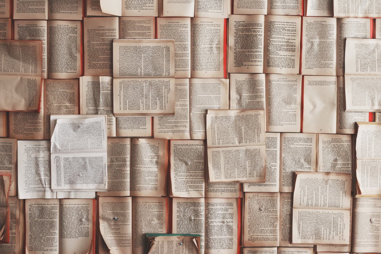 Dozens of books are opened to show their words are spread across the floor, placed side by side, you are looking down on them from above.