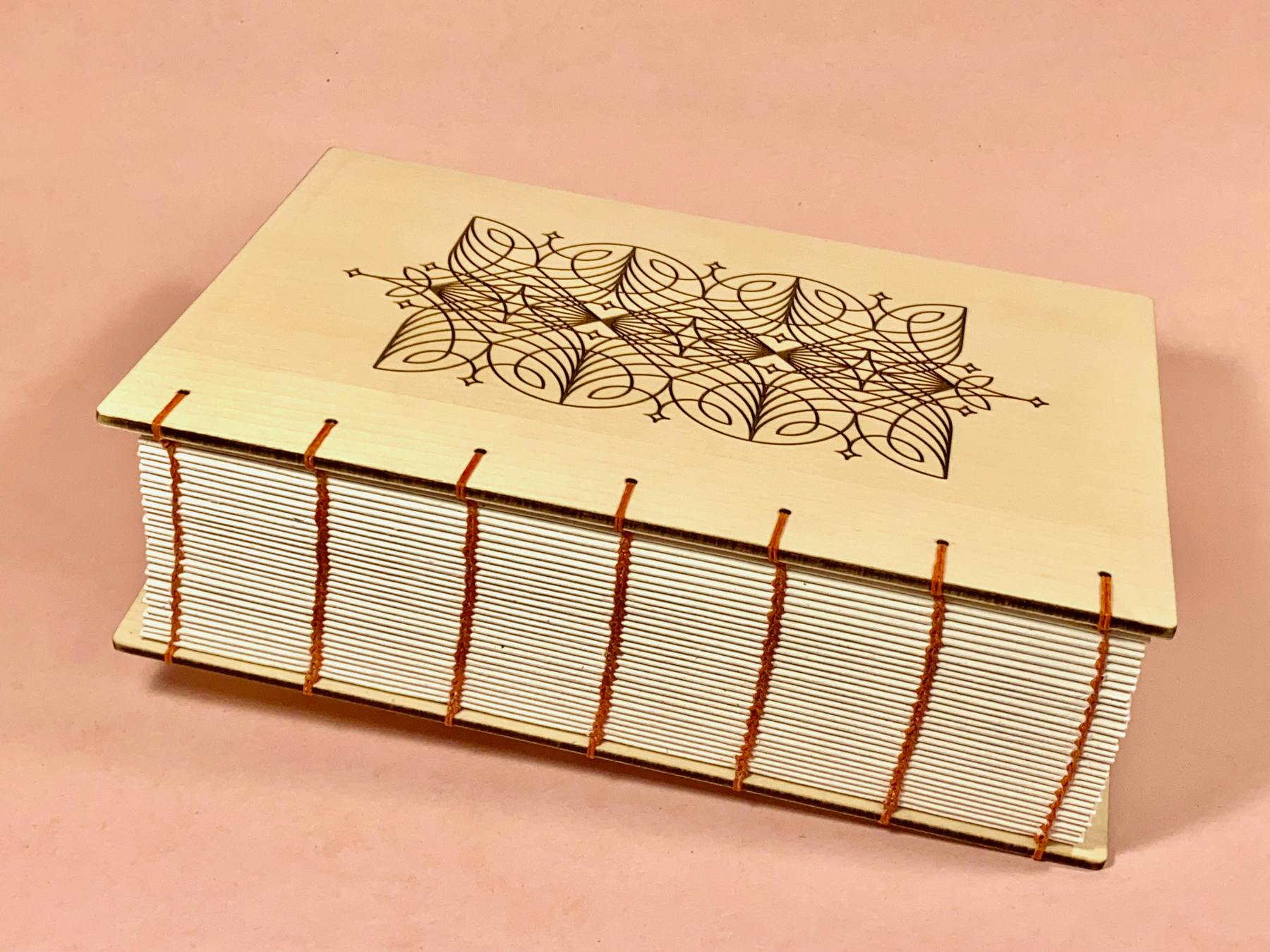 A thickkk coptic-bound Maple Fondfolio book with exposed red linen thread lays horizontally on a rose pink background, the left corner is tilted slightly so the book appears to be floating up. We created this book for a customer who ordered a Fondfolio for her own 40th birthday after her celebrations were cancelled due to COVID. 240 people contributed, which at the time was the most we’d ever seen in one book. The contributions were also of a really high calibre — top quality words! It’s engraved with a custom design inspired by words her friends said about her being a connector — a joyful bringer together of like-hearted humans.