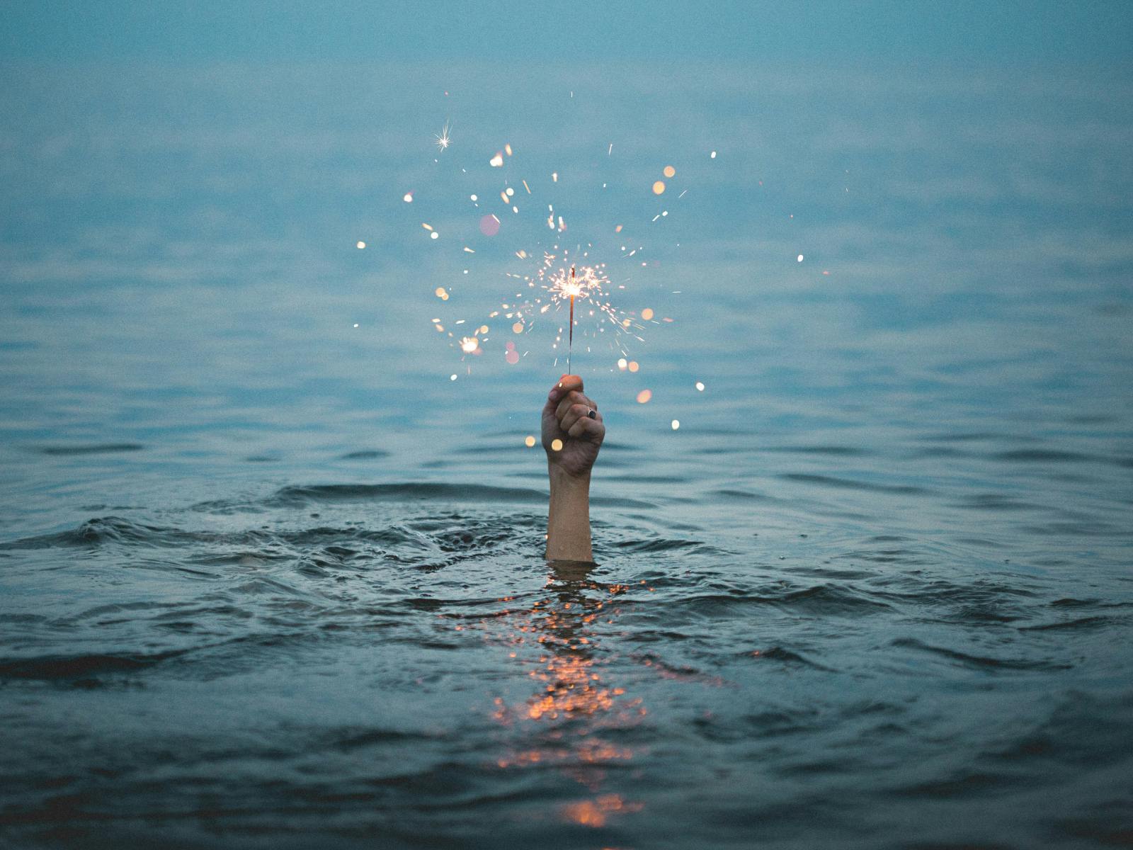 A lone hand holding a lit sparkler rises above calm water