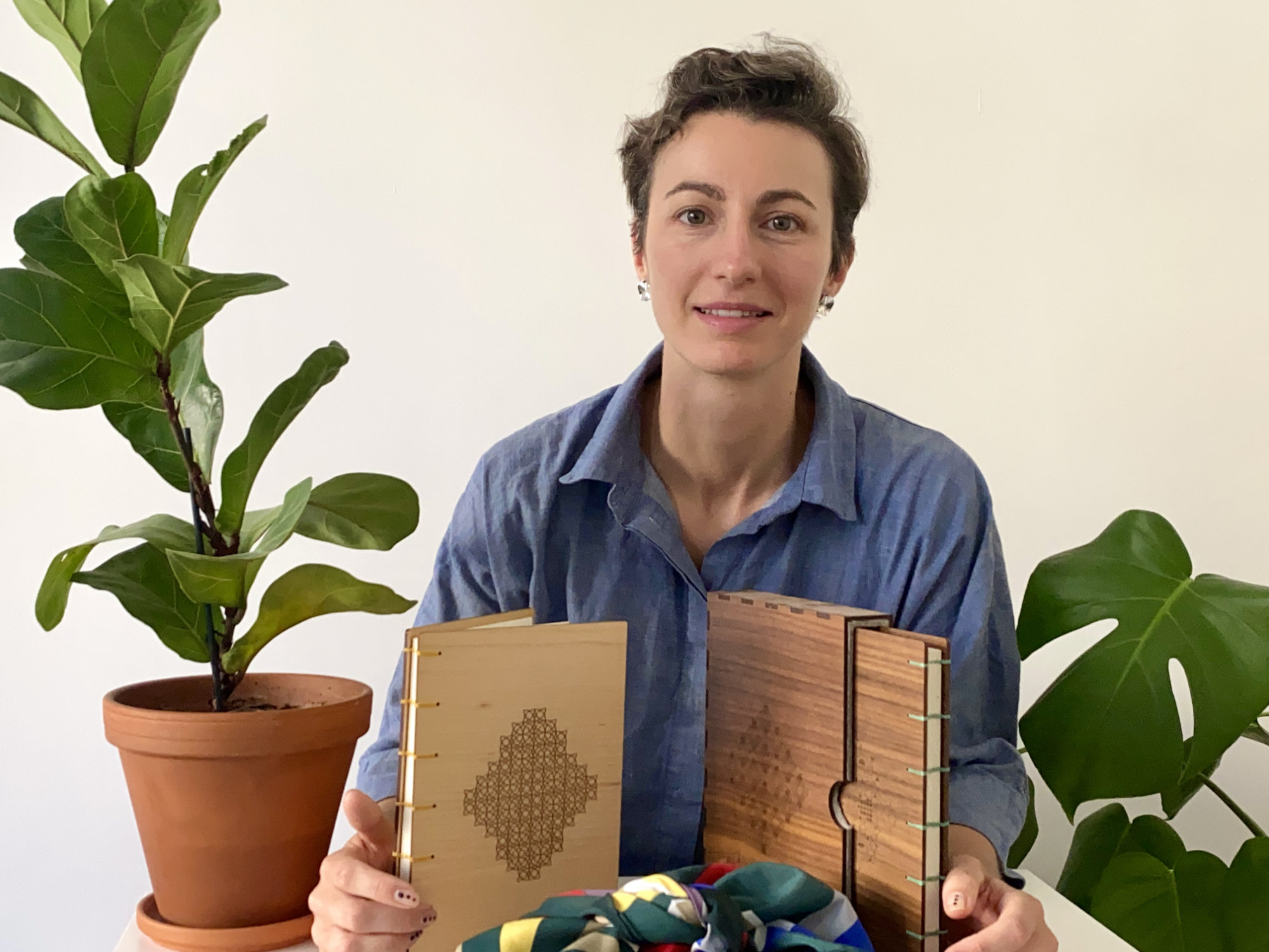 Me behind a desk in between two plants holding two Fondfolio books, one maple and one walnut.