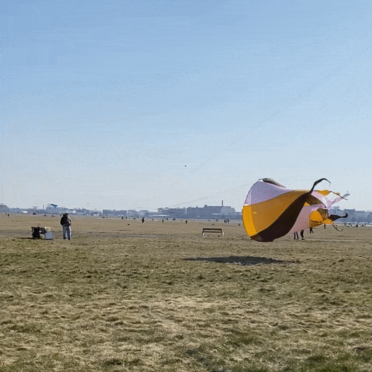 A massive low-flying Vortex kite. A funnel shape, striped pale pink orange and burgundy, the kite spins in the wind.