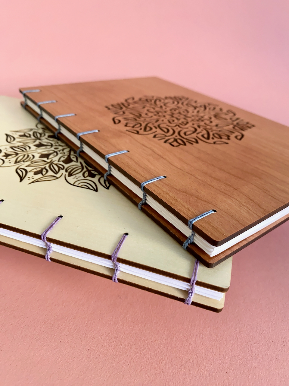 Two Fondfolio books against a pink background. One is made of Maple wood and the other of Cherry wood.