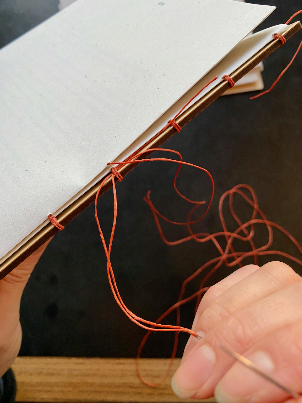 A closeup shot of my hands sewing a book, showing the speckletone paper and vibrant red waxed-linen thread.