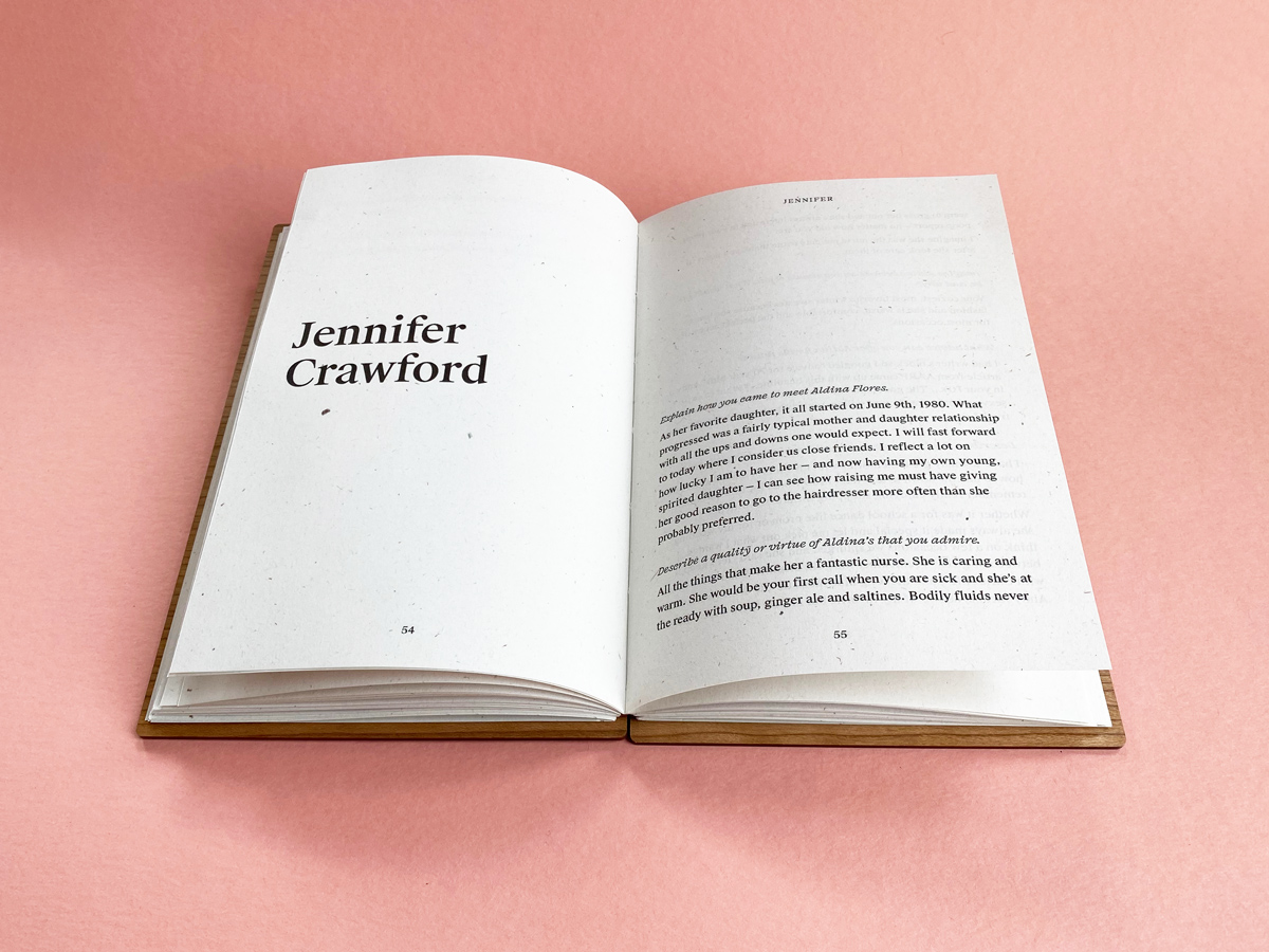 A Fondfolio book with a walnut wood cover lays open against a rose pink background. The contributor’s name is printed in the middle of the left page set in bold serif type and their words appear on the right.